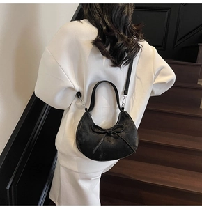 Détail du sac demi-lune en cuir noir mat avec nœud, porté en bandoulière sur mannequin