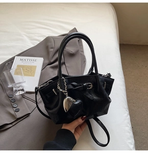 Detalle de bolso cubo negro mate con colgante de corazón pulido y correa larga