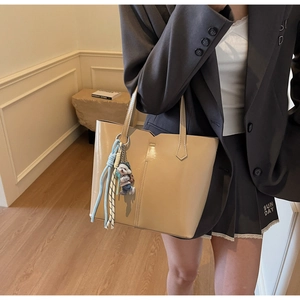 Detail of beige glossy leather tote bag with charm on grey suit and pleated skirt