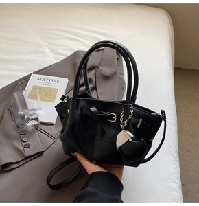 Detalle de bolso tipo cubo en cuero negro brillante con colgante de corazón y bandolera