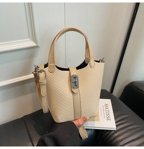 Detail of beige bucket bag with woven texture and silver metal clasp on black leather
