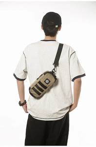 Close-up of khaki waterproof chest bag with black straps and Earth logo patch detail