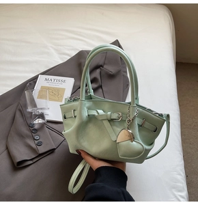 Detalle del bolso tipo cubo verde menta con colgante de corazón y hebilla decorativa