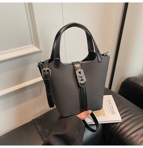 Detail of grey woven bucket bag featuring black leather handles and silver metal clasp