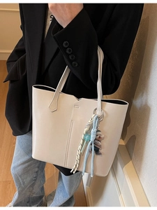 Minimalist beige tote bag with shoulder straps and dog charm shown on a model