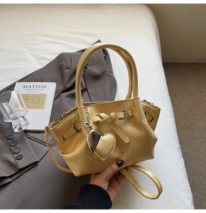 Detalle de bolso tipo cubo amarillo pálido con colgante de corazón en cama blanca
