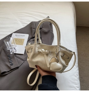 Detalle del bolso tipo saco crema con hebilla metálica, colgante de corazón y cuero PU