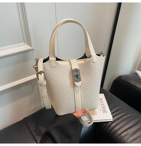 Detail of cream woven bucket bag with leather handle and adjustable crossbody strap