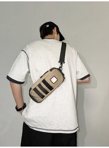 Close-up of khaki cylindrical crossbody bag with reflective square patch and nylon strap