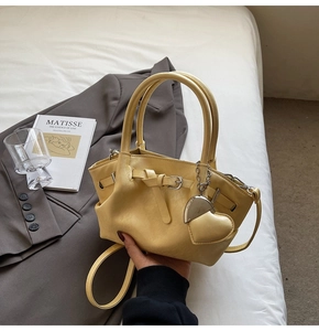 Primer plano del bolso cubo de cuero amarillo con colgante de corazón y correa ajustable