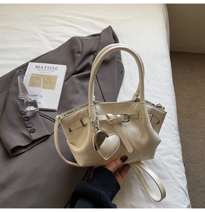Detalle de bolso saco crema con colgante de corazón y correa de hombro ajustable