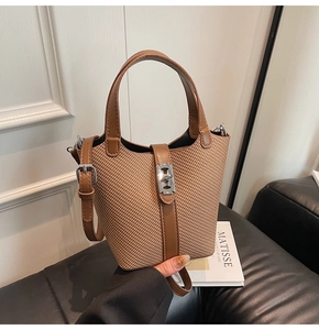 Detail of woven bucket bag featuring brown leather trim and metallic H buckle closure