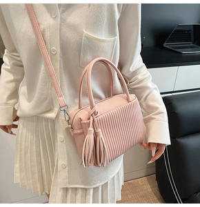Detail of pink lychee leather crossbody bag featuring stylish tassels and pleated texture