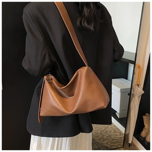 Détail du sac bandoulière en cuir marron porté par un mannequin en costume décontracté