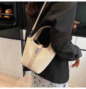 Detail of beige straw bucket bag with silver metal lock and leather strap in lifestyle setting