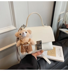 Detail of white glossy square handbag with a cute brown plush bear charm and silver clasp