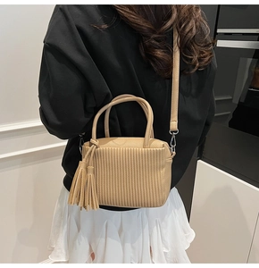 Detail view of beige crossbody bag with vertical pleats and decorative long fringe tassel