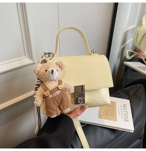 Detail of cream patent leather square handbag featuring a cute plush teddy bear charm
