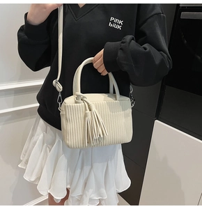 Close-up of beige ribbed handbag featuring side tassel charm and slim adjustable shoulder strap