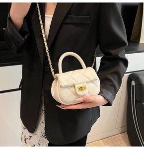 Dettaglio mini borsa trapuntata bianca con chiusura dorata e tracolla a catena su blazer