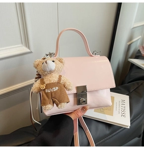 Detail of light pink crossbody square bag with silver clasp and plush bear charm accessory
