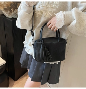 Detail of black crossbody bag with vertical pleated texture and tassel charm on model