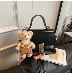 Close-up of black glossy leather handbag featuring silver twist lock and teddy bear charm