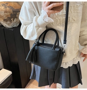 Detail of black pleated Boston bag with tassel charm and textured synthetic leather