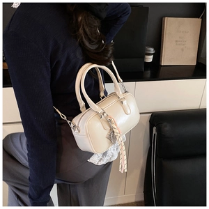 Detailansicht einer cremefarbenen Boston-Tasche mit Metallanhängern und schmalem Schultergurt