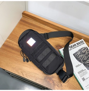 Tactical black chest bag with reflective patch and MOLLE webbing on wood table