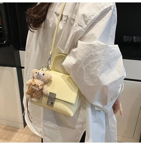 Detail van lichtgele gestructureerde crossbodytas met pluche berenhanger en zilveren slotje