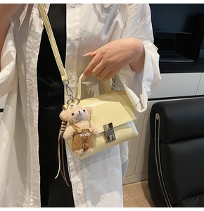 Detail of cream square crossbody bag with silver twist lock and plush bear pendant