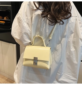 Detail van een minimalistische crème crossbodytas met zilveren gesp gedragen door model