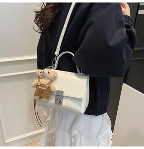 Detail of white leather crossbody bag with silver twist lock and teddy bear charm