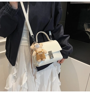 Detail van witte crossbodytas met een schattige teddybeerhanger aan de schouderriem