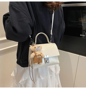 Detail van crème crossbodytas met zilveren sluiting en een schattige pluche beer