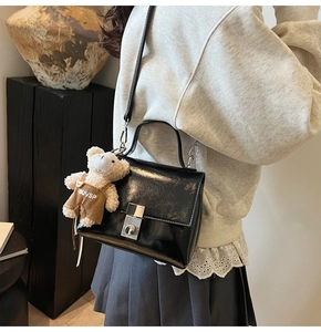 Detail of black glossy handbag with silver square lock and a cute teddy bear charm