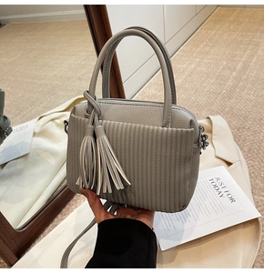 Detail of grey lychee texture handbag featuring a pleated pocket and decorative tassel