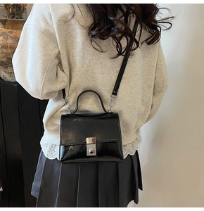 Detail van een zwarte glanzende crossbodytas met zilveren slot gedragen door model