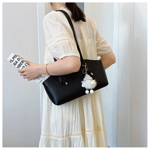 Detail of a large black leather shoulder bag with a cute white plush charm on a model
