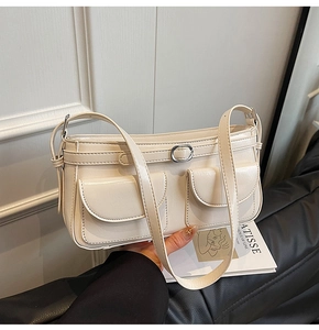 Détail du sac crème avec deux poches et boucle ronde argentée sur la sangle en cuir souple