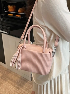 Pink lychee leather crossbody bag with pleated texture and side tassels in home setting