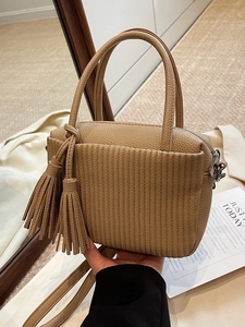 Chic khaki pebbled leather crossbody bag with dual tassels and top handles in a warm setting