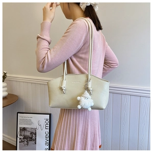 Detail of minimalist cream underarm bag with smooth texture and cute plush pendant
