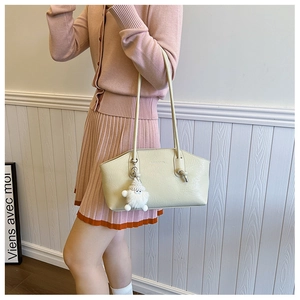 Detail of light beige tote bag with litchi texture and cute white plush pendant