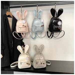 Detail of five mini rabbit-ear backpacks in glossy synthetic leather with plush charms