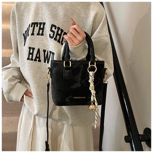 Detail of black glossy leather bucket bag with gold hardware and striped ribbon accessory