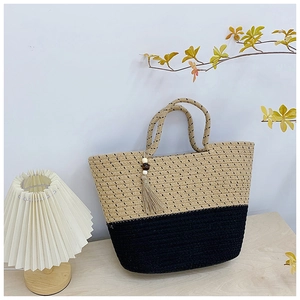 Detail of bicolor woven straw tote bag with black contrast and wood bead tassel charm