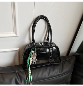 Détail du sac bowling noir brillant avec logo de marque et breloque ours argentée