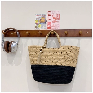 Detail of hand-woven two-tone straw tote bag with elegant tassel hanging on wooden hook